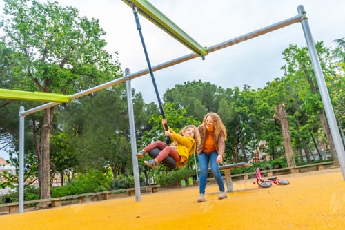 Preview: Full length of mother swinging a girl on a park