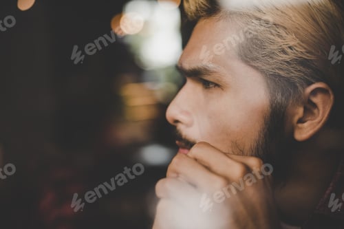 Preview: Pensive young hipster man sitting in coffee shop thinking and looking away.