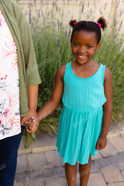 Preview: Portrait of african american girl holding hands of her granddaughters while standing outdoors