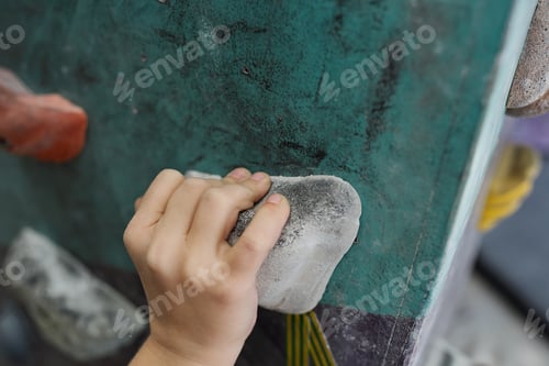 Preview: Hand of schoolboy on one of small rocks of climbing equipment