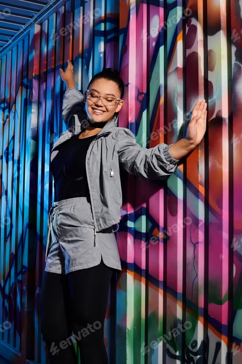 Preview: Stylish woman poses confidently against vibrant graffiti backdrop in urban setting