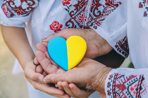 Preview: Grandmother holds in her hands a heart in the color of the Ukrainian flag. Selective focus.