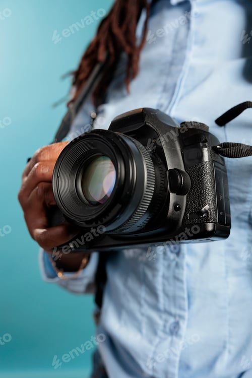 Preview: Close up of young adult photograhpy entusiast holding a modern camera device while standing on blue