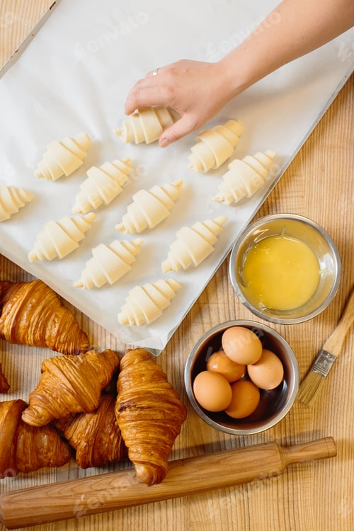 Preview: Raw rolled up and freshly baked croissants as well as ingredients lie on the table.