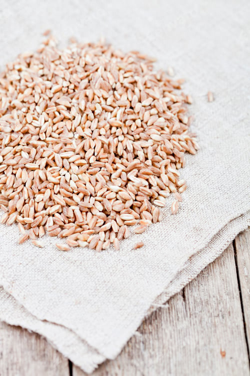 Preview: Dry raw organic wheat grain heap on linen tablecloth on rustic wooden table background.