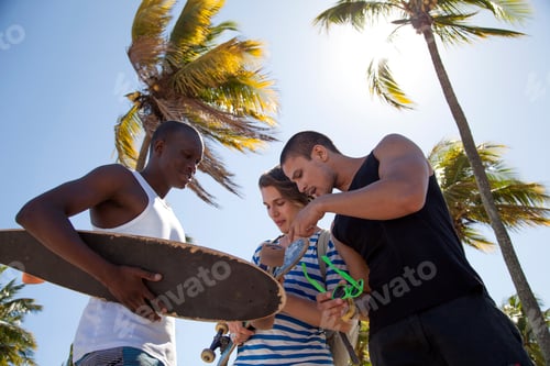Preview: Young man holding skateboard with friends, low angle
