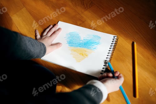Preview: A small refugee boy from Ukraine with a drawing of the Ukrainian flag.