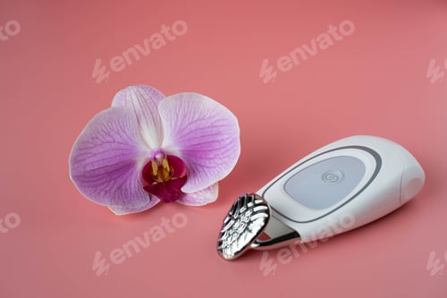 Preview: Closeup shot of an orchid flower and a wrinkle iron spa tool isolated on the coral background