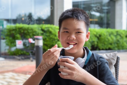 Visualização: Menino tailandês comendo sorvete de baunilha com calda de chocolate ao ar livre