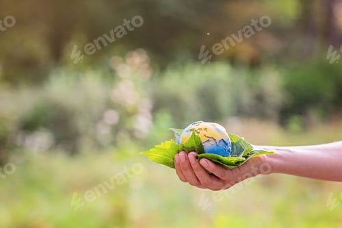 Preview: Young woman holding small planet in hands against spring or summer green background