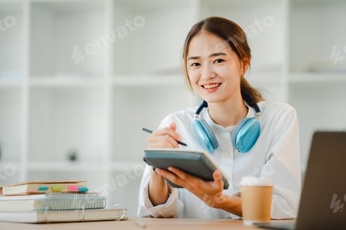 Preview: Beautiful Asian female student with a cheerful smile Wearing headphones, studying online and taking