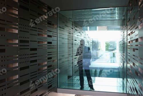 Preview: Germany, Cologne, Businessman standing behind glass door, using mobile phone