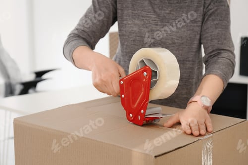 Preview: Young woman packing moving box indoors, closeup
