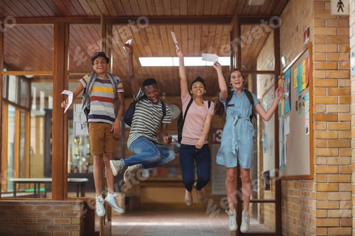 Preview: Excited classmates jumping with grade cards in corridor