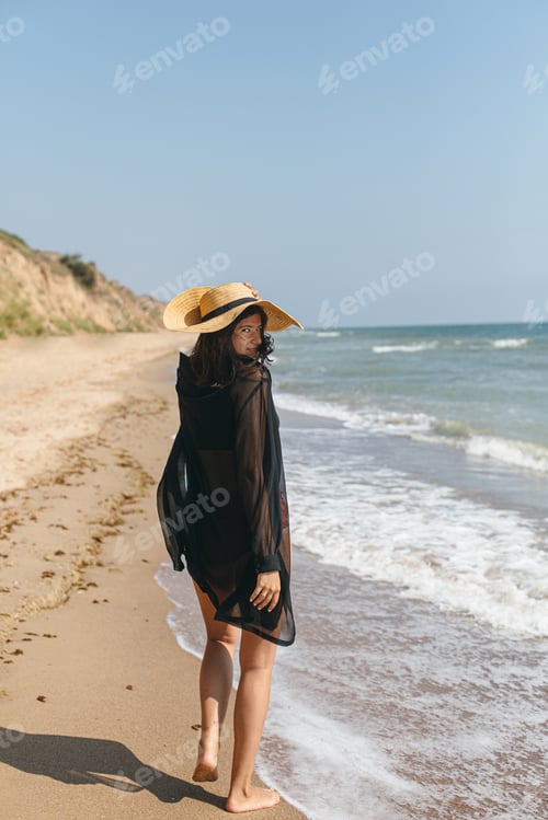 Vista previa: Summer vacation. Beautiful stylish woman with hat walking on sandy beach at sea waves and relaxing