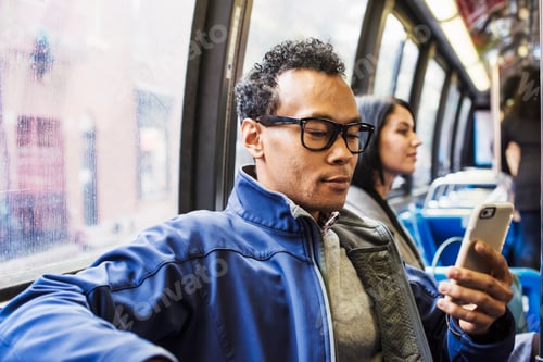 Preview: A young man and a young woman sitting on public transport looking at their cellphones.