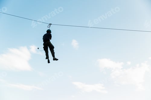 Preview: A silhouette of a man on a zip line against a blue sky