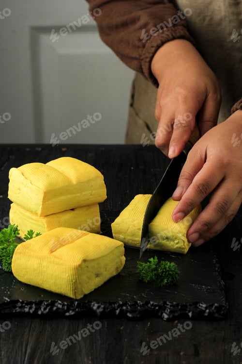 Preview: Yellow Tofu Slice using Sharp Knife by Female Chef. Selected Focus Bean Curd on Ceramic Black Plate