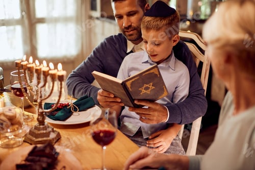 Preview: Small Jewish boy and his father reading Tanakh at dining table during Hanukkah.