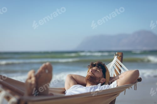 Preview: Front view of handsome young Caucasian man relaxing on hammock at beach on a sunny day