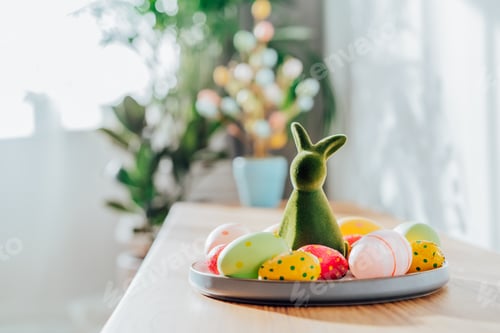Preview: Easter home decor. Green bunny rabbit figurine and colored easter chocolate eggs on plate
