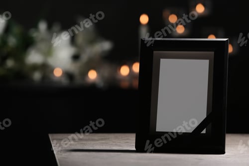 Preview: Funeral photo frame with black ribbon on table in dark room