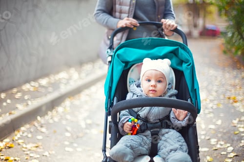 Preview: Young blond woman with stroller going for a walk in a park