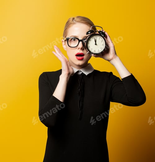 Preview: Surprised woman in black formal clothes with alarm clock on yellow background