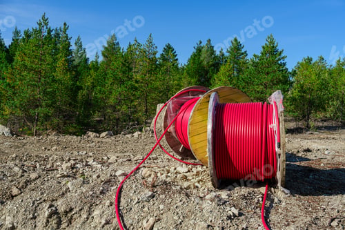Preview: Wooden Reel with High Voltage Red Cable in Forest: Ready for Underground Power Line Installation