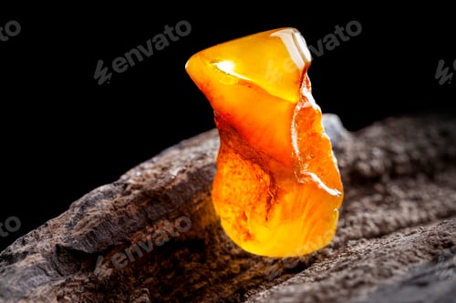 Preview: Natural amber. A piece of yellow opaque natural amber on large piece of dark stoned wood