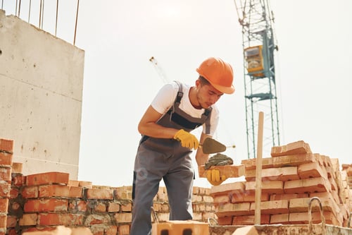 Preview: Young construction worker in uniform is busy at the unfinished building