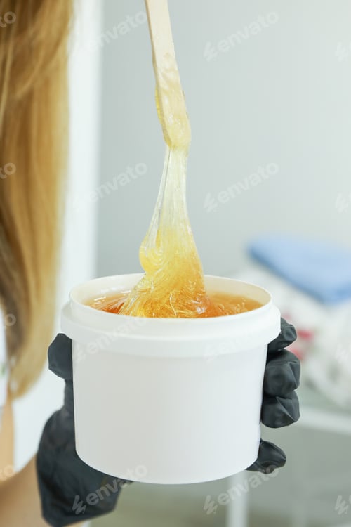Preview: Woman holding liquid yellow paste for shugaring against white background, close up
