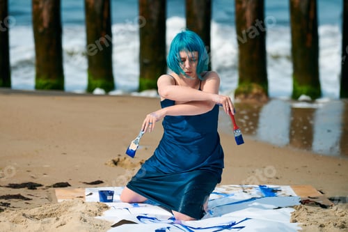 Preview: Artistic blue-haired woman performance artist smeared with gouache paints on large canvas on beach