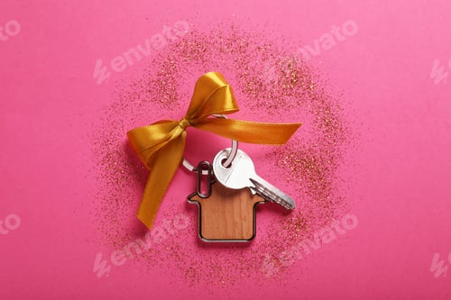 Preview: Key with trinket in shape of house, bow and glitter on pink background, flat lay. Housewarming party