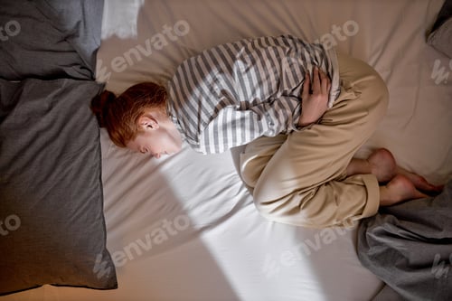Preview: Top view of sick young ginger redhead woman lying in bed