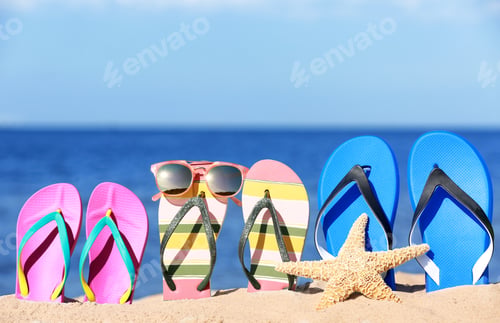 Preview: Composition with bright flip flops on sand near sea in summer. Beach accessories