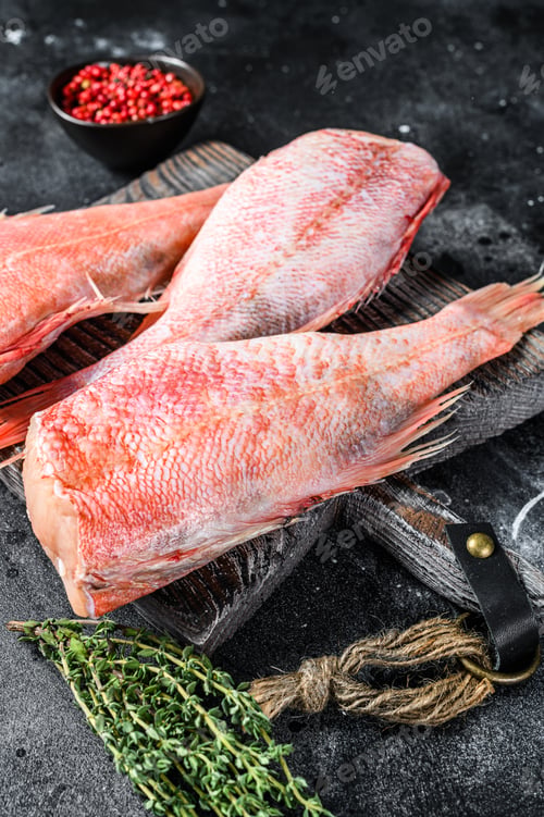 Preview: Raw Red perch or seabass fish on a cutting board. Black background. Top view