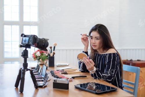 Preview: Asian woman blogger with makeup cosmetics recording video clip by smartphone at home.