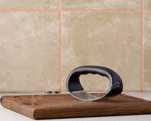 Preview: Hand held metal garlic press on a wooden cutting board