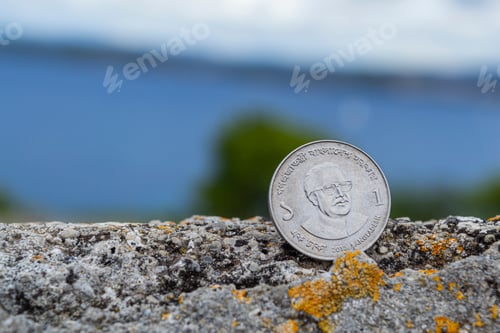 Preview: Bangladesh coin on a rustic wall with seascape in a background