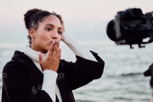 Preview: Pretty African American girl happily sending air kiss on camera during photo session by the sea
