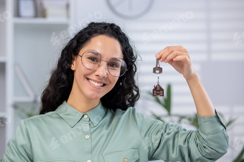 Preview: Smiling woman holding house key with keychain in a home office