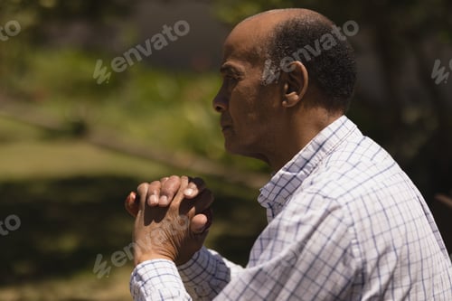 Preview: Thoughtful senior man hands leaning on a cane while sitting on bench on sunny day in garden