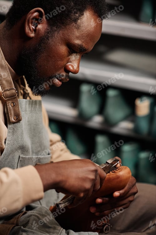 Preview: Side view of young African American man in apron creating new boot or shoe