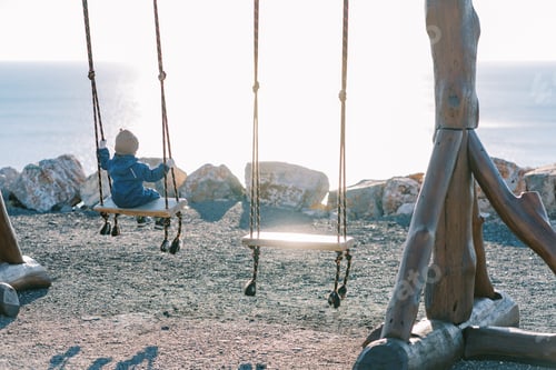 Preview: Little girl swings on a large rope swing on the seashore. Back view