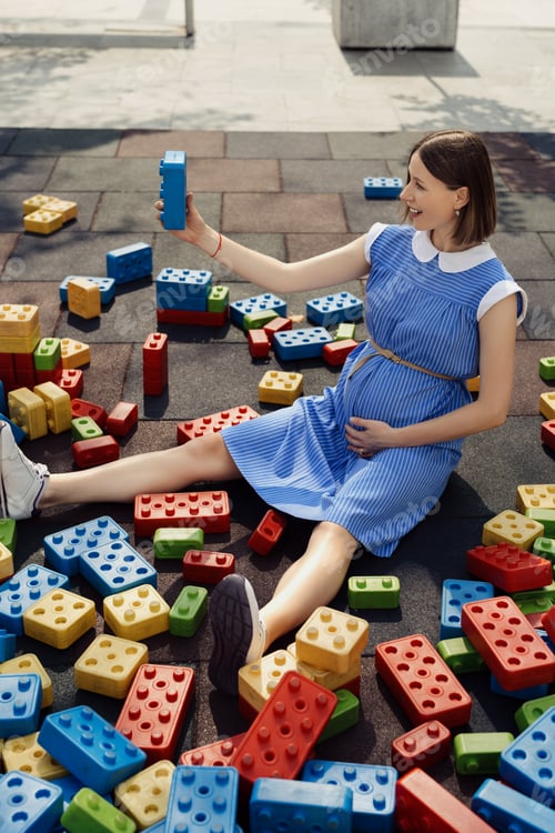 Preview: Happy pregnant woman among colorful toy cubes
