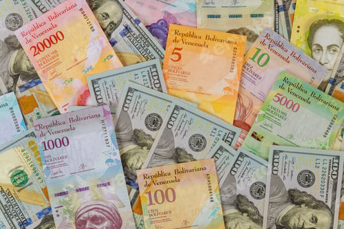 Preview: American dollar bills notes over Venezuelan Bolivar banknote with paper currency bills.