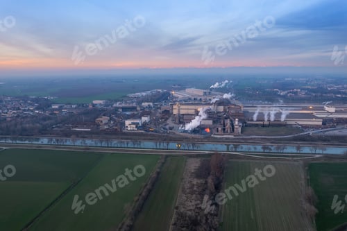 Preview: Industrial factory emitting large amounts of smoke into the air in a green field at sunset