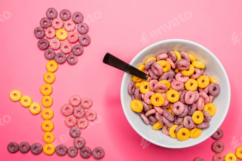 Preview: Top view of a cereal bowl with the cereal pieces aligned in a shape of a flower on pink background