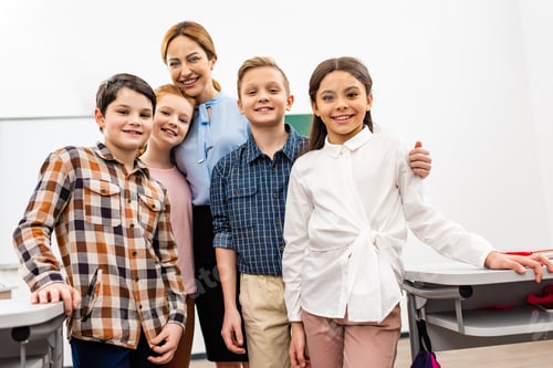 Visualização: Professor rindo com alunos em pé na sala de aula e olhando para a câmera